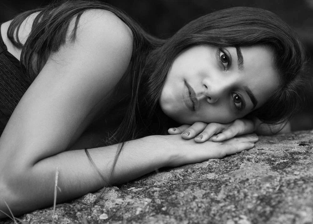 Black and white photo of a teenage girl laying with her head on her hand, gazing into the camera